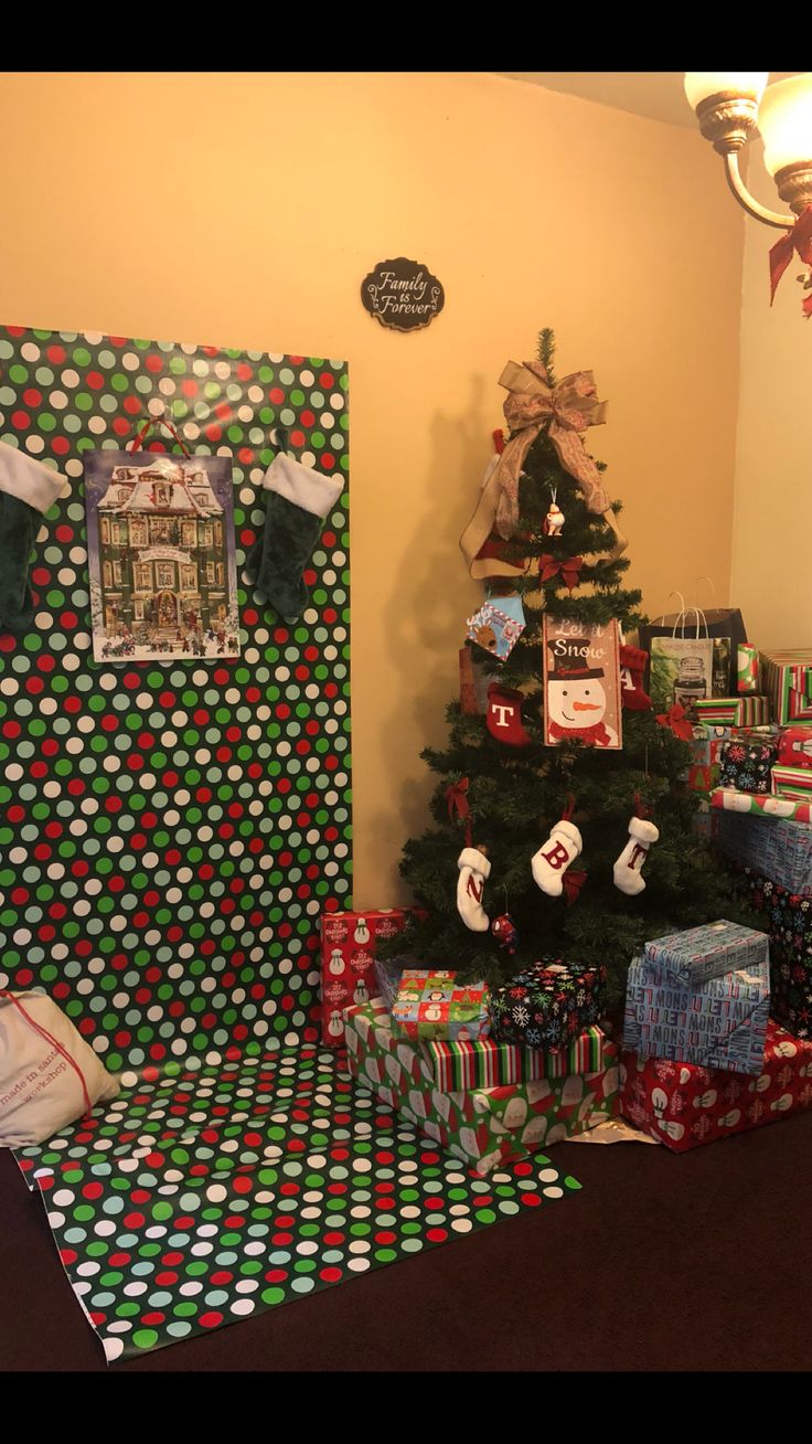 a christmas tree with presents under it in front of a wall covered in wrapping paper