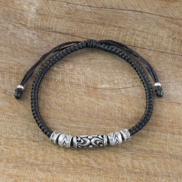 The Karen hill tribe artisans from Thailand are known for making jewelry unique to their corner of the world. Artisan Napapat comments that their works are ...very creative and beautiful but also distinctly Thai: their methods unchanged from mother to daughter. Here she presents a hand braided ebony colored cord bracelet with a barrel-shaped silver tube flanked on each side by two beads; the detailing of the tube's filigree motif and the bead's decorations is further enhanced by the combination Traditional Adjustable Bracelet With Wooden Beads, Traditional Adjustable Wooden Beads Bracelet, Traditional Adjustable Wooden Bead Bracelet, Artisan Black Festival Bracelet, Artisan Black Bracelet For Gift, Unique Adjustable Bracelet With Black Beads, Unique Black Bracelets For Festivals, Handmade Black Spiritual Leather Bracelet, Traditional Handmade Adjustable Leather Bracelet