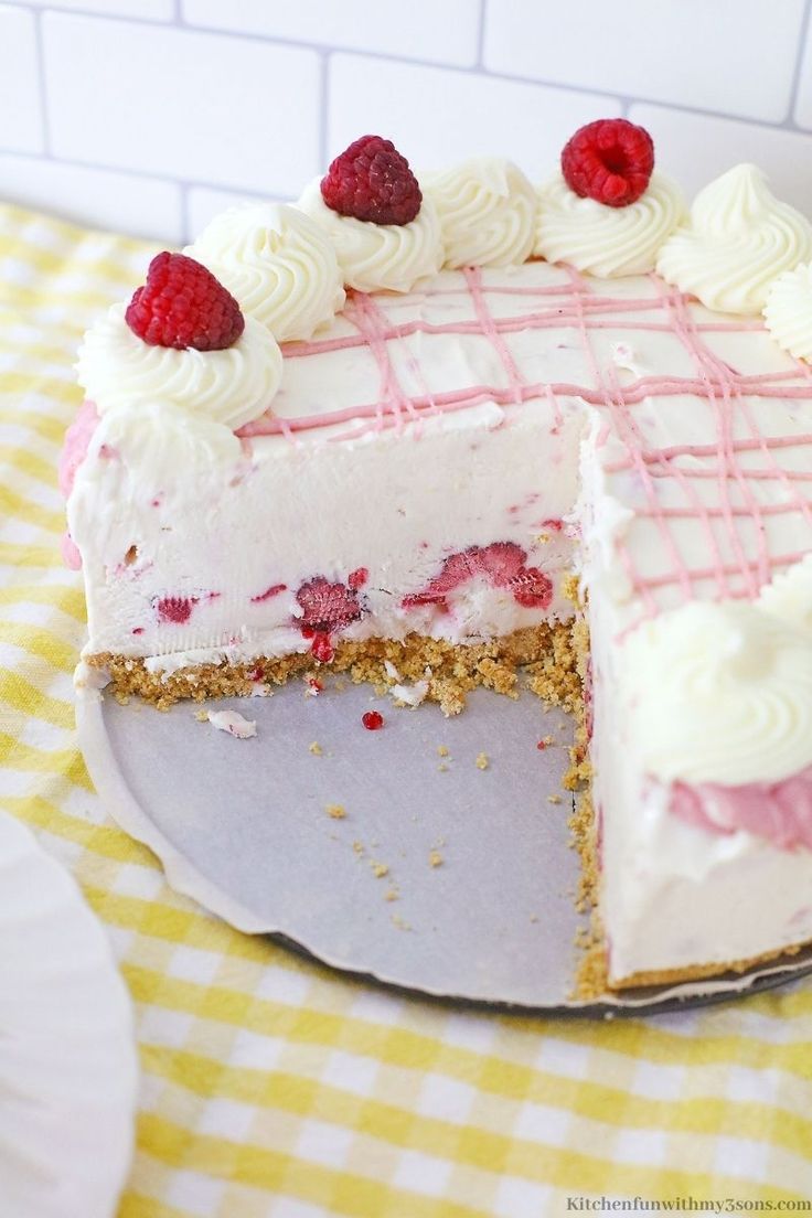 a white cake with raspberries on top is sitting on a yellow and white checkered tablecloth