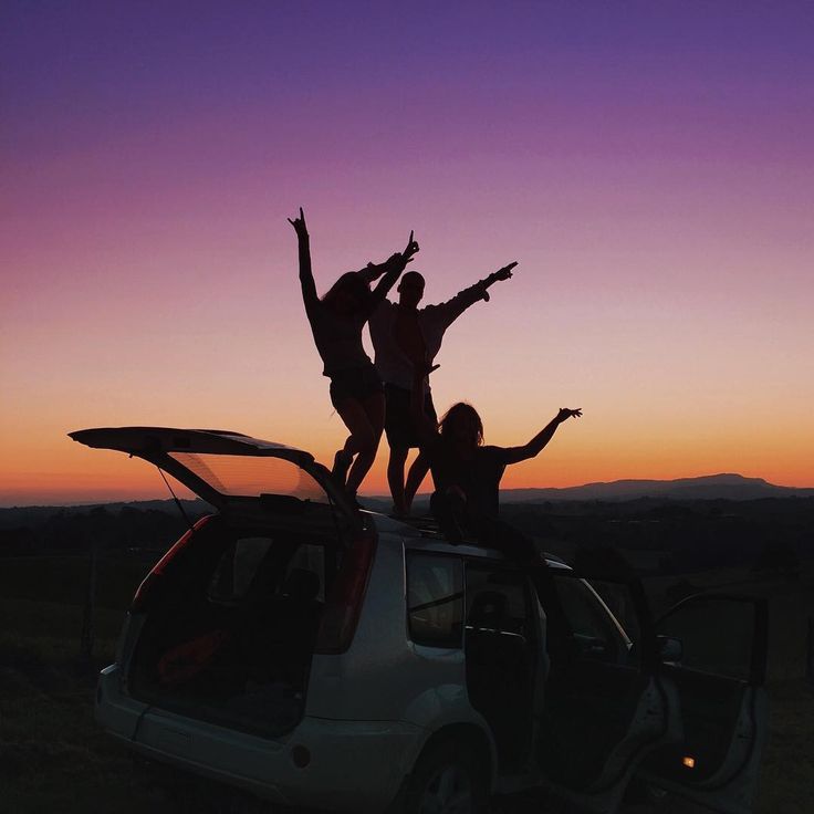 three people standing on the roof of a car with their arms up in the air