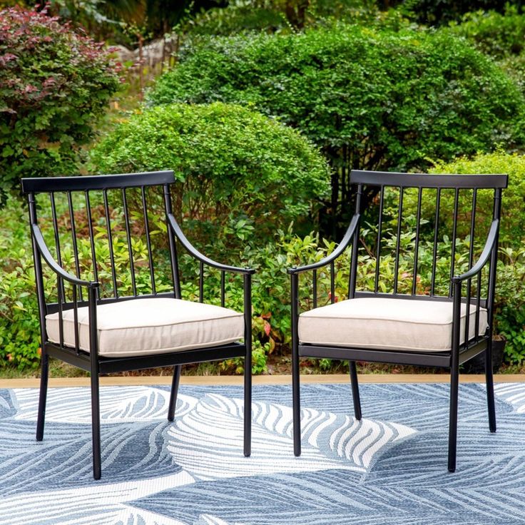 two black chairs sitting on top of a blue and white rug in front of bushes