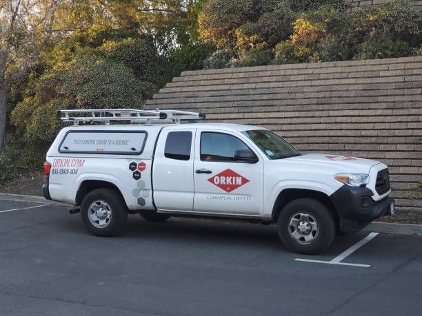 a white truck parked in a parking lot next to a wooden wall and trees with no leaves on it