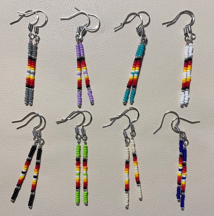 six pairs of multicolored beaded earrings hanging from hooks on a white surface