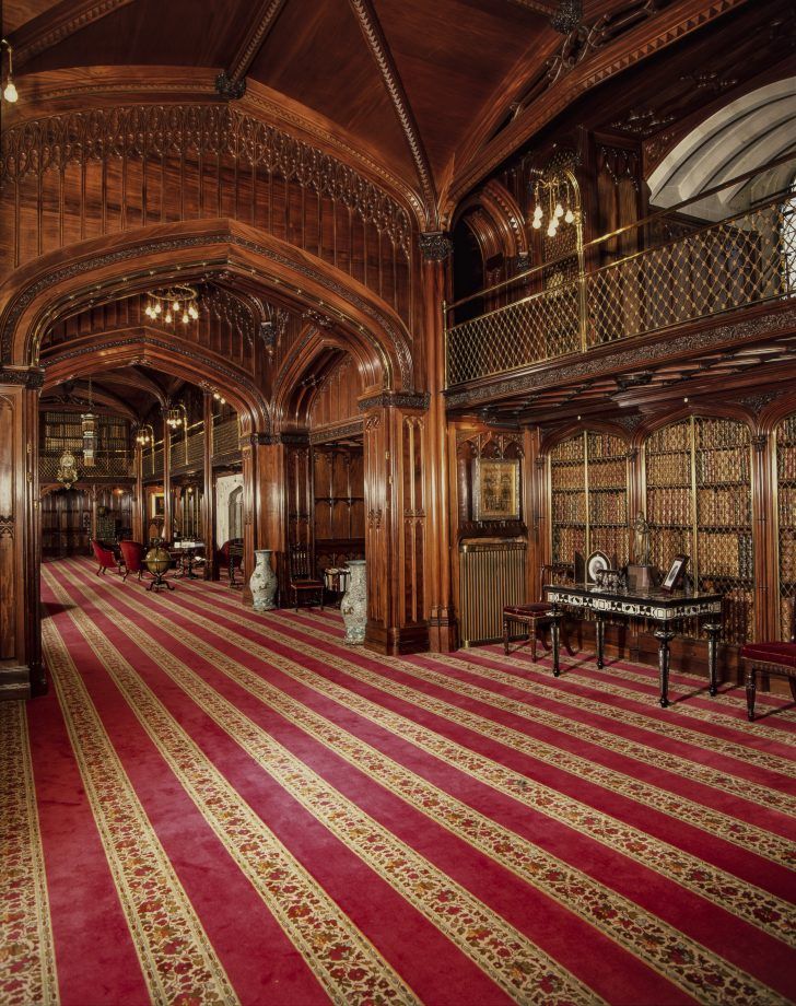 an ornately decorated library with red and gold carpeting, chandeliers and tables