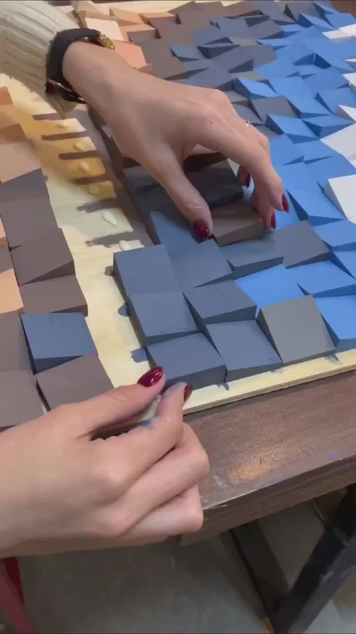 This may contain: two hands are working on some blue and gray tiles with one hand reaching for the tile