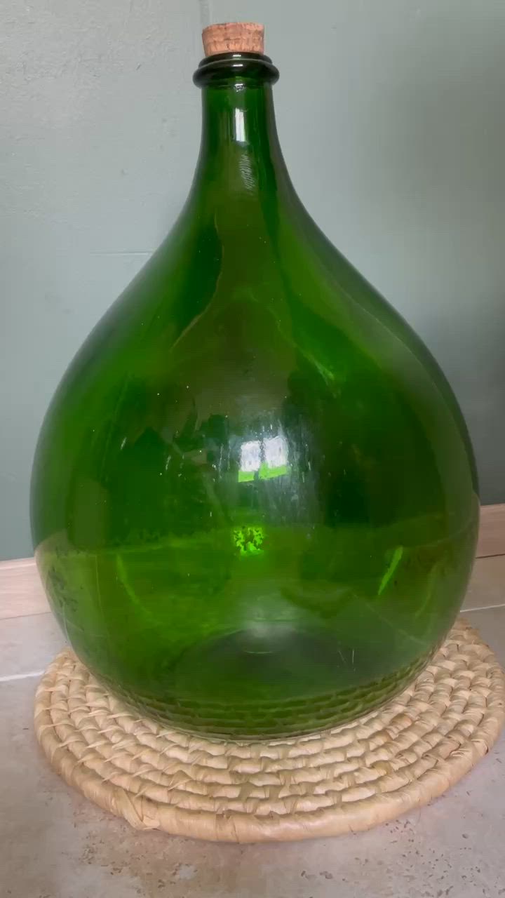 This may contain: a person holding a large green vase with white string on it's top and bottom