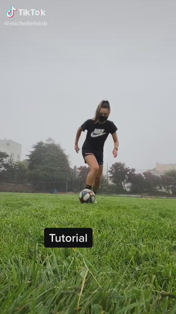 This may contain: a woman kicking a soccer ball across a lush green field