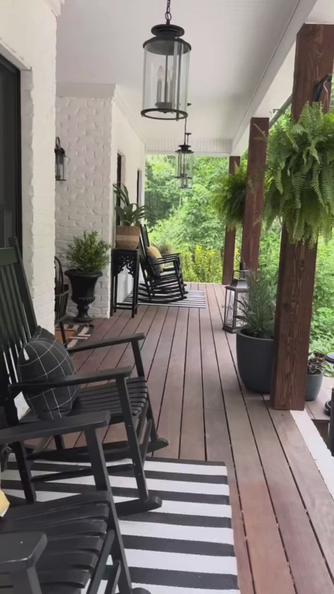 This may contain: a porch with black rocking chairs and potted plants on the back deck, surrounded by greenery