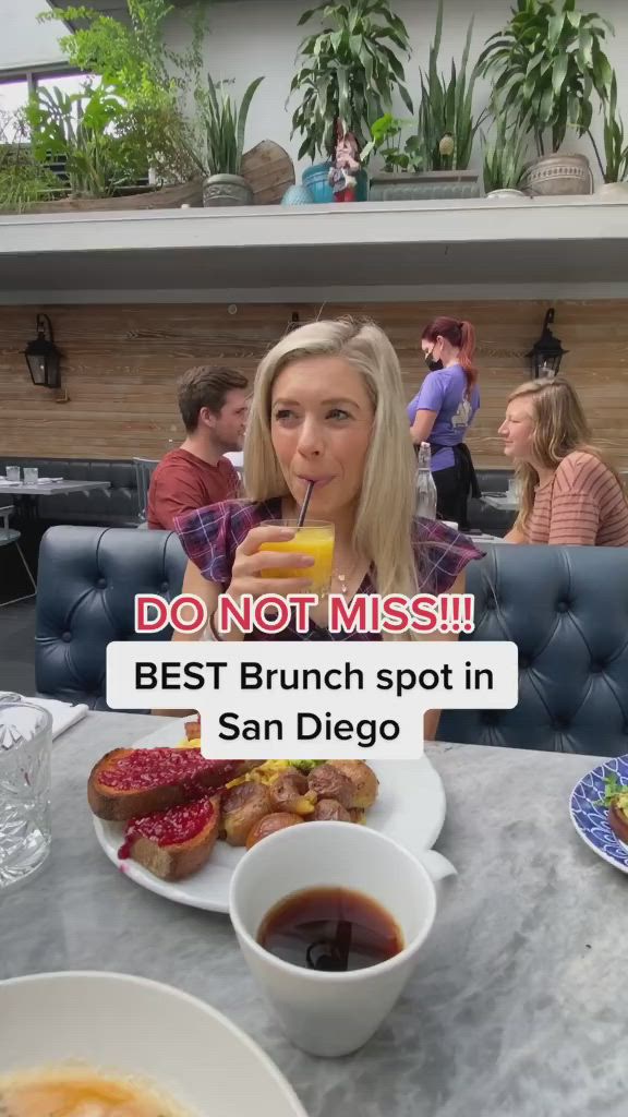 This may contain: a woman sitting at a table with food in front of her and the words do not miss best brunch spot in san diego