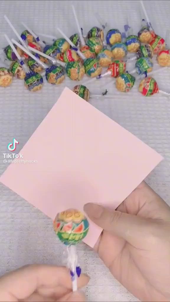 This may contain: a person holding a candy lollipop in front of a pink piece of paper