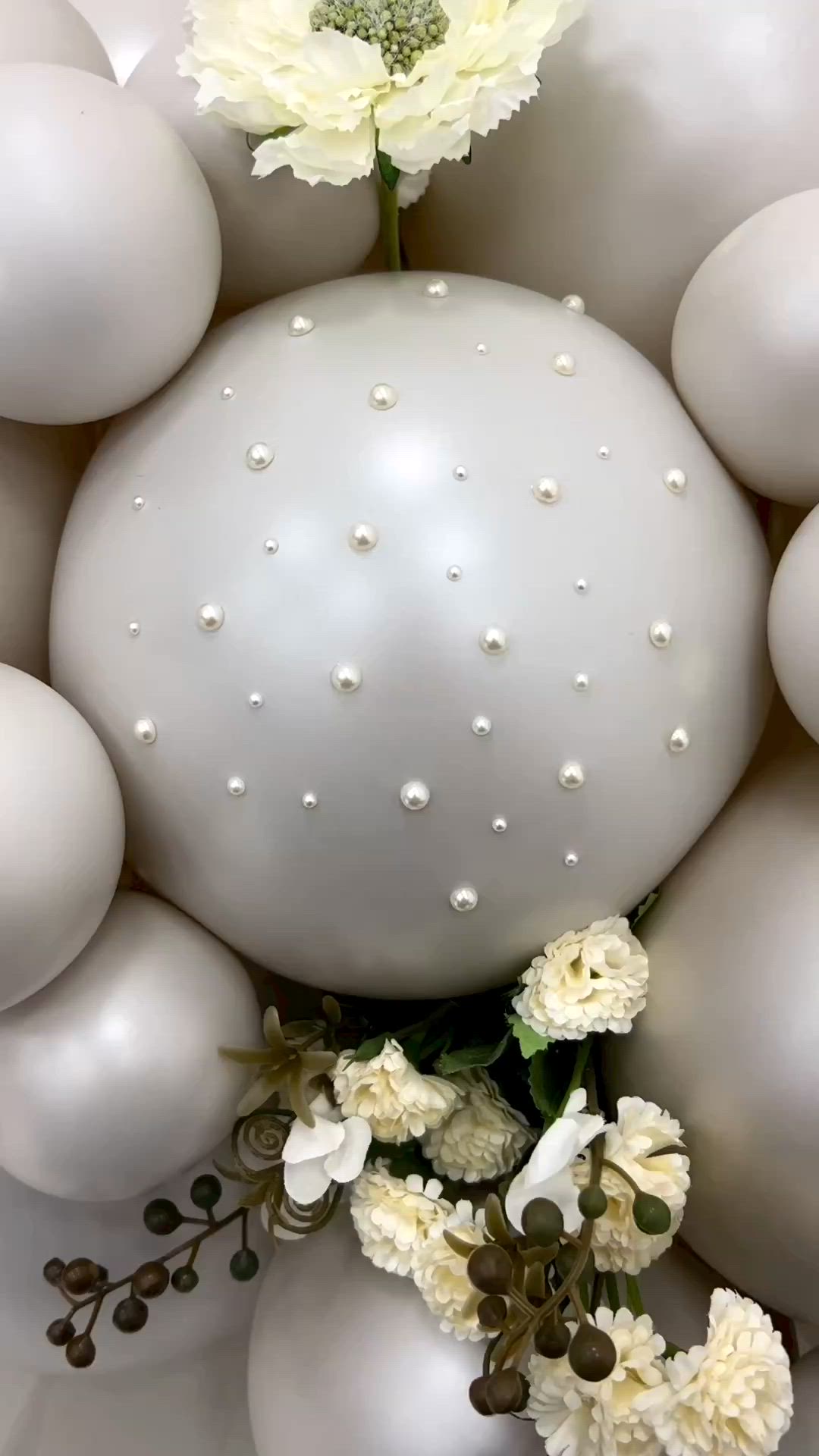 This may contain: an arrangement of white balloons with flowers and pearls on the bottom one is surrounded by smaller balls