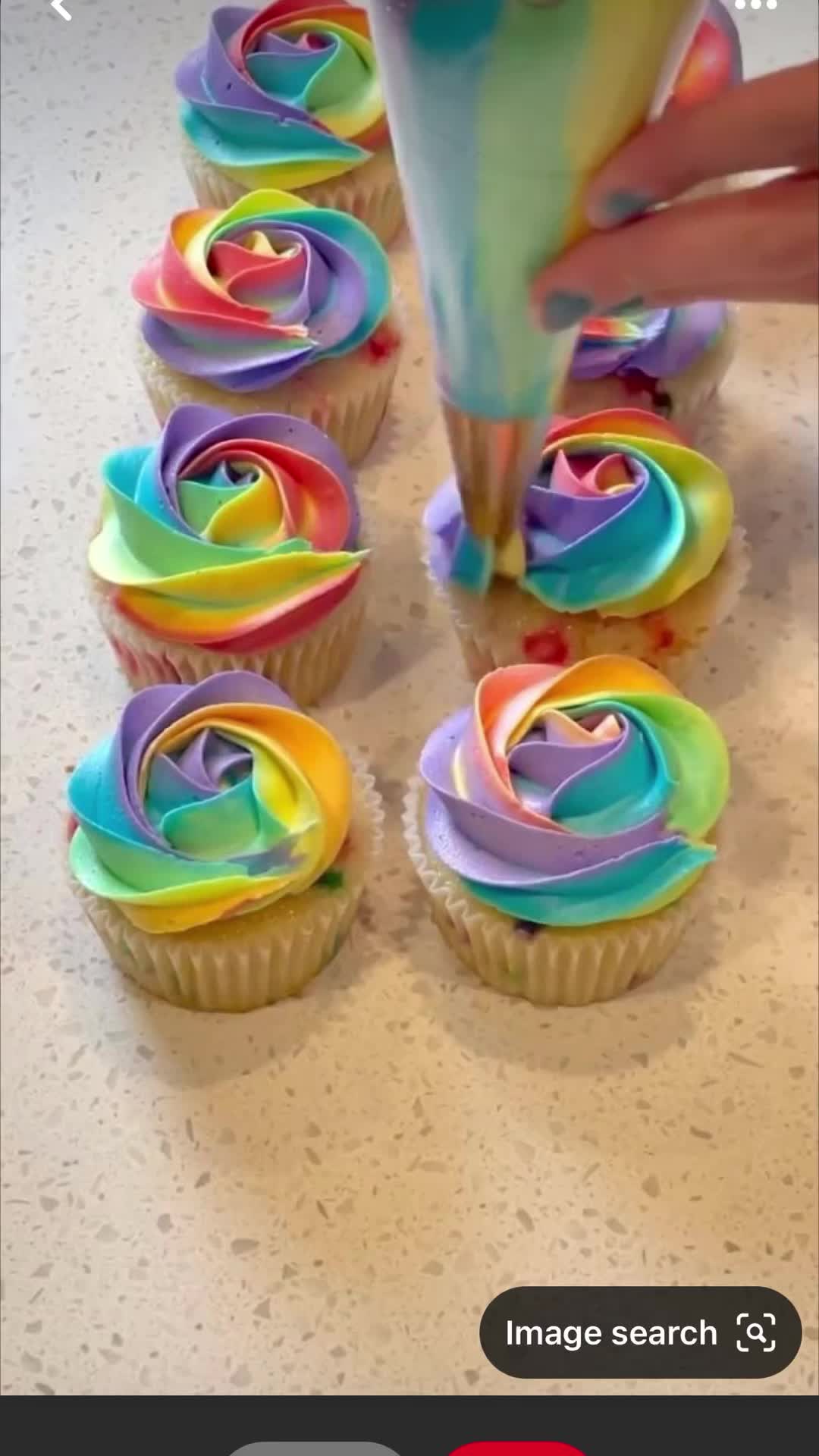 This may contain: someone is decorating cupcakes with rainbow icing on the top and bottom