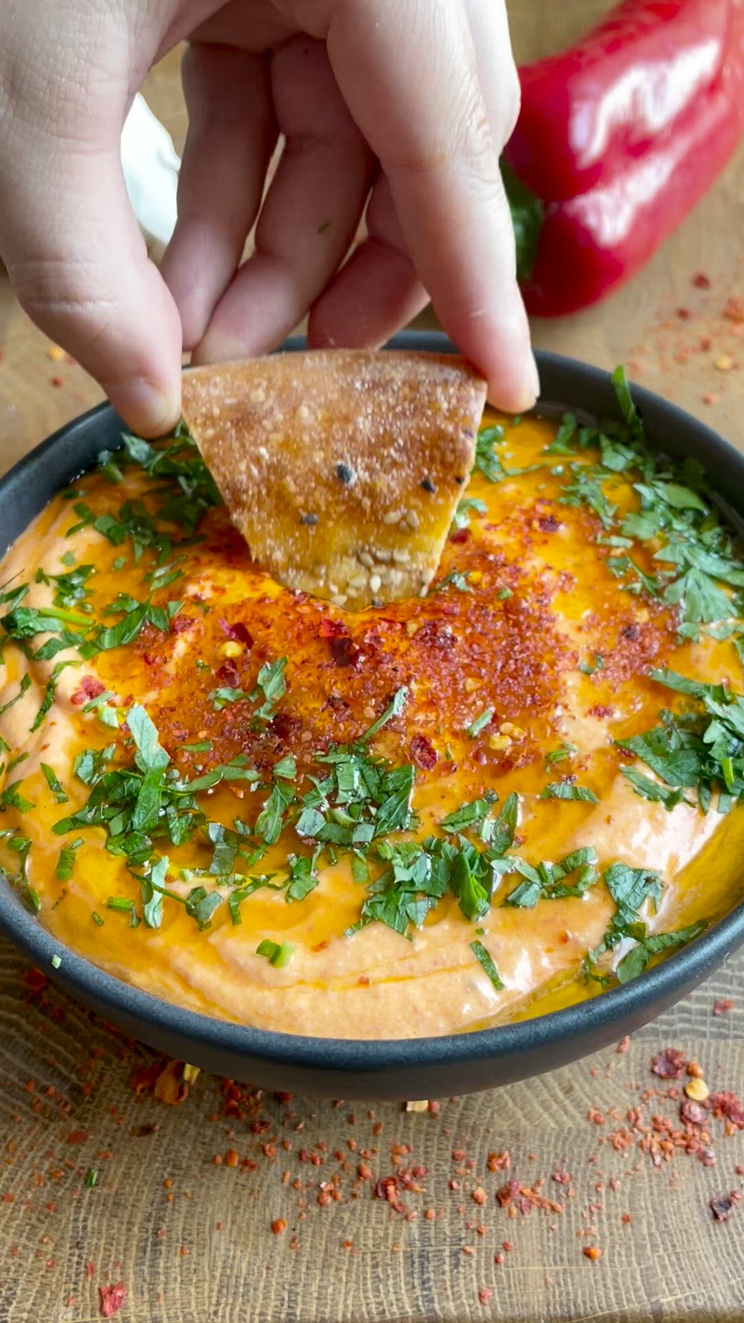 This may contain: a hand dipping a tortilla chip into a bowl filled with sauce and cilantro