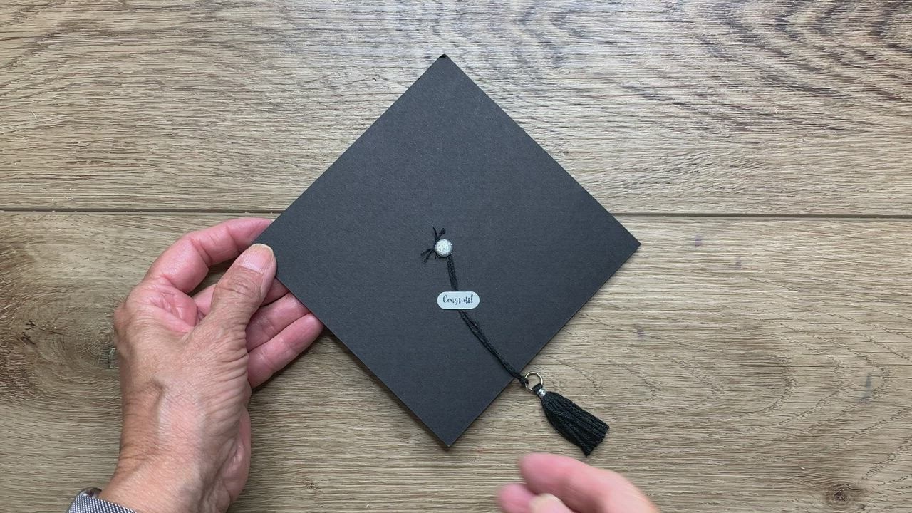 This may contain: a person holding a graduation cap on top of a wooden table next to another hand