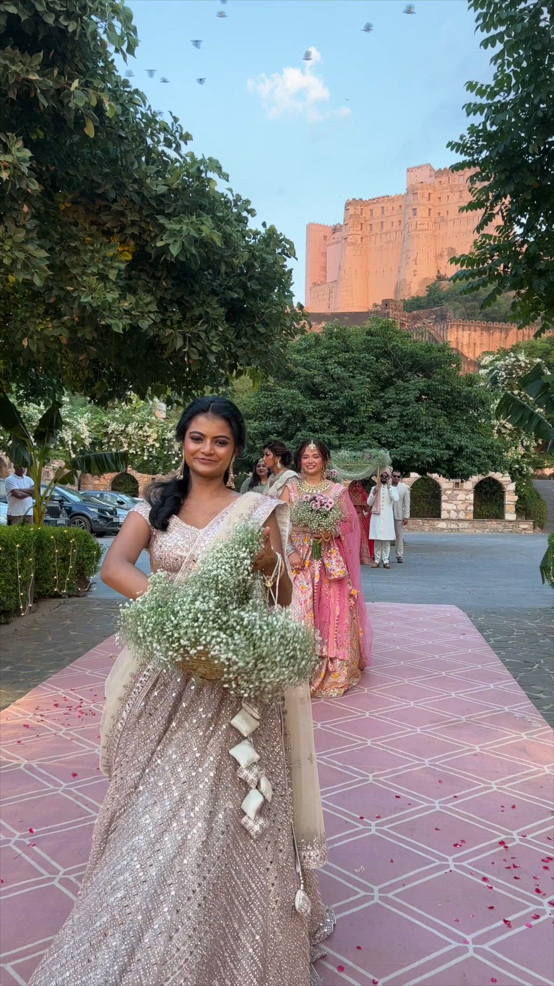 This may contain: a woman in a white and silver dress is holding flowers while another woman stands behind her