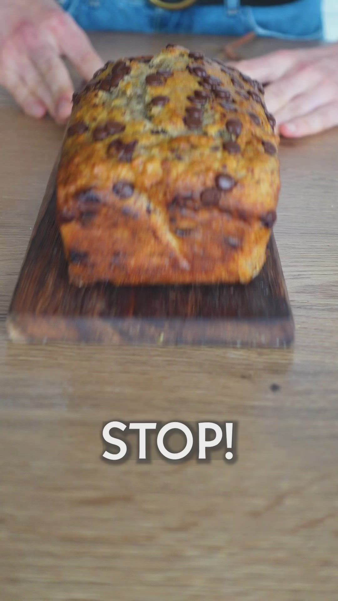 This may contain: a loaf of bread sitting on top of a wooden table next to a person holding a knife