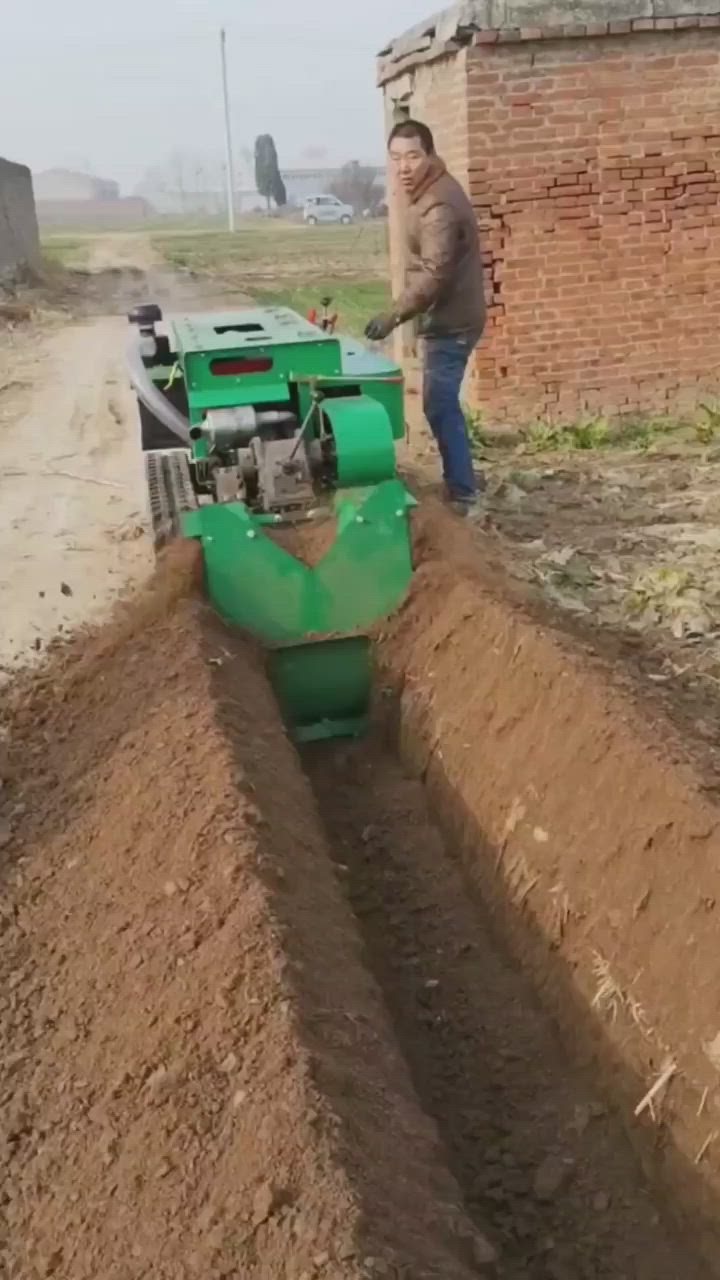 This may contain: a man standing next to a green machine in the middle of a dirt field near a brick building