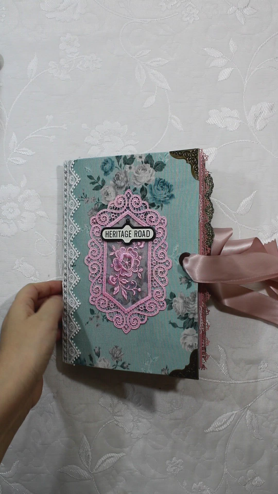 This may contain: a hand holding a pink ribbon over a blue and white book with an ornate design