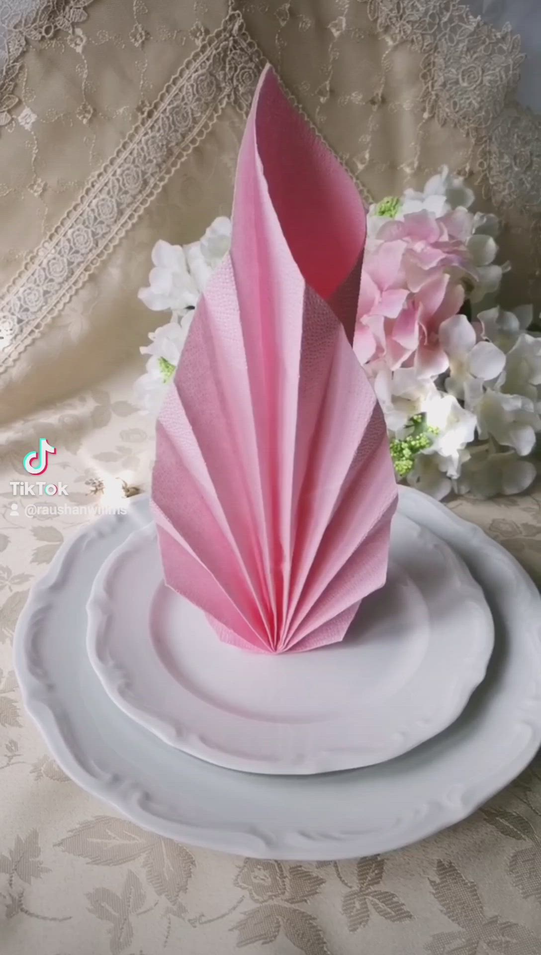 This may contain: a pink folded paper umbrella sitting on top of two white plates next to some flowers