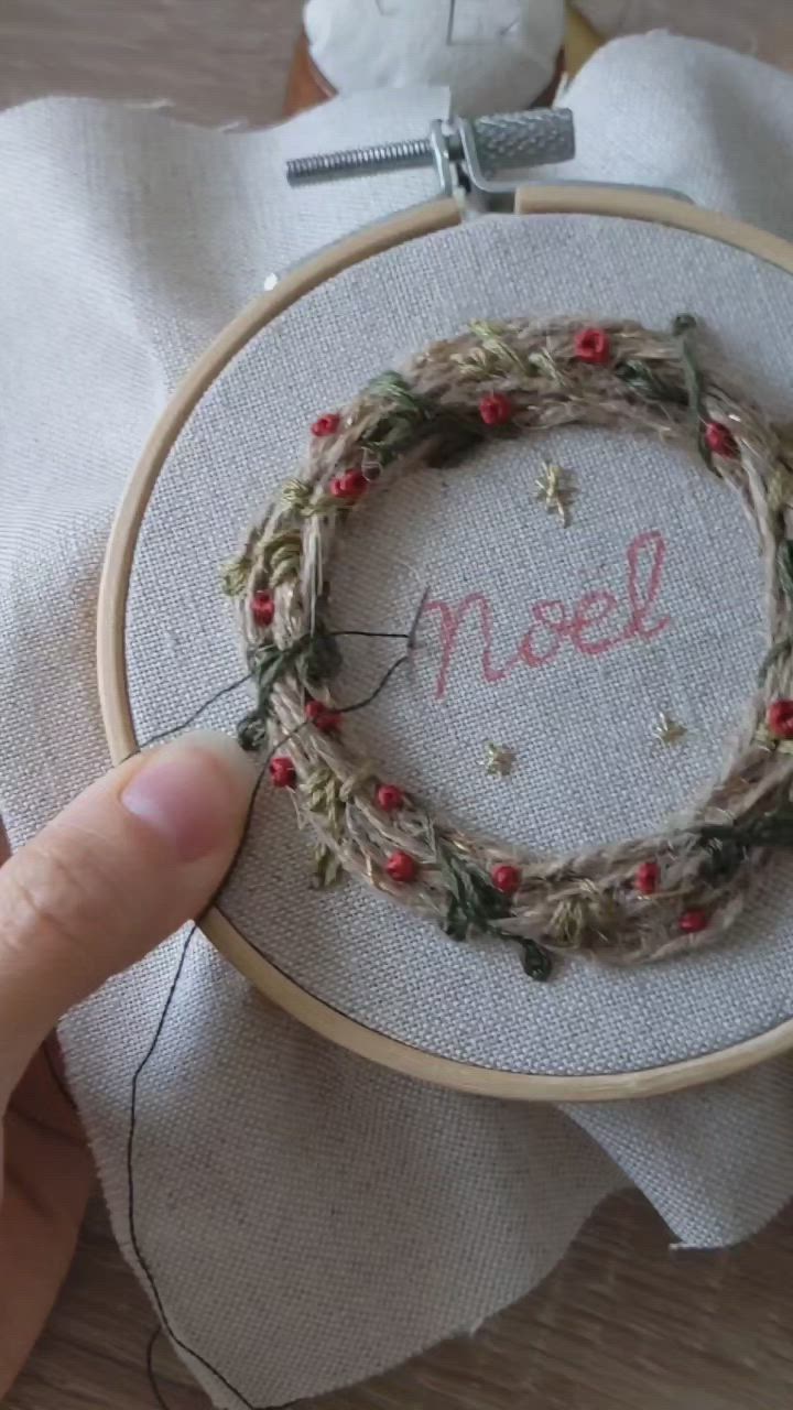 This may contain: someone holding up a hand embroidered wreath with the word noel on it