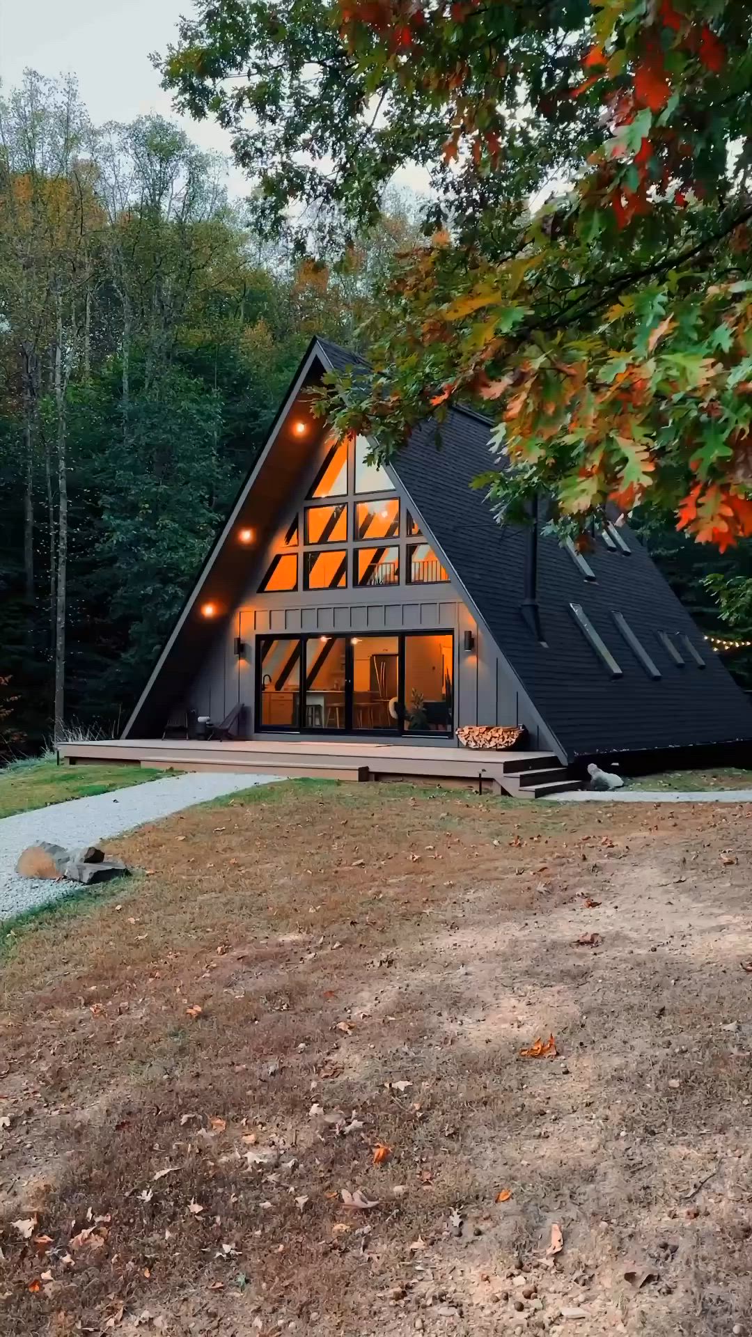 This may contain: a - frame cabin in the woods with lights on it's windows and stairs