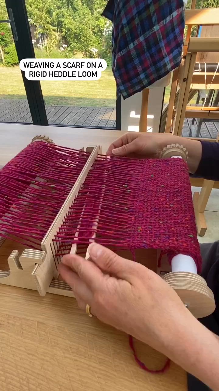 This may contain: two people working on weaving at a table with chairs in the background and text overlay that reads weaving a scarf on a rug heddle loom