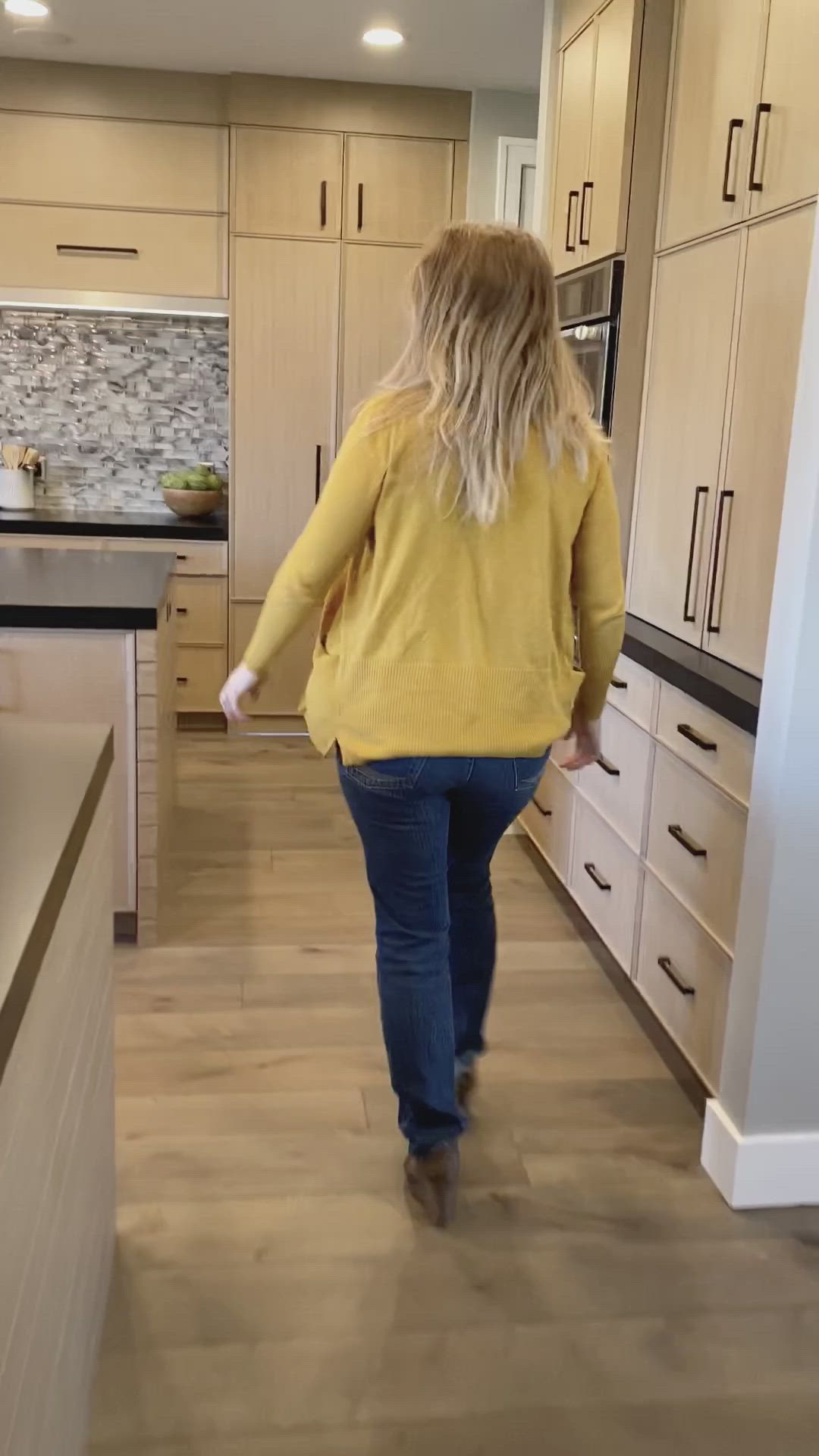 This may contain: a woman walking through a kitchen with white cabinets