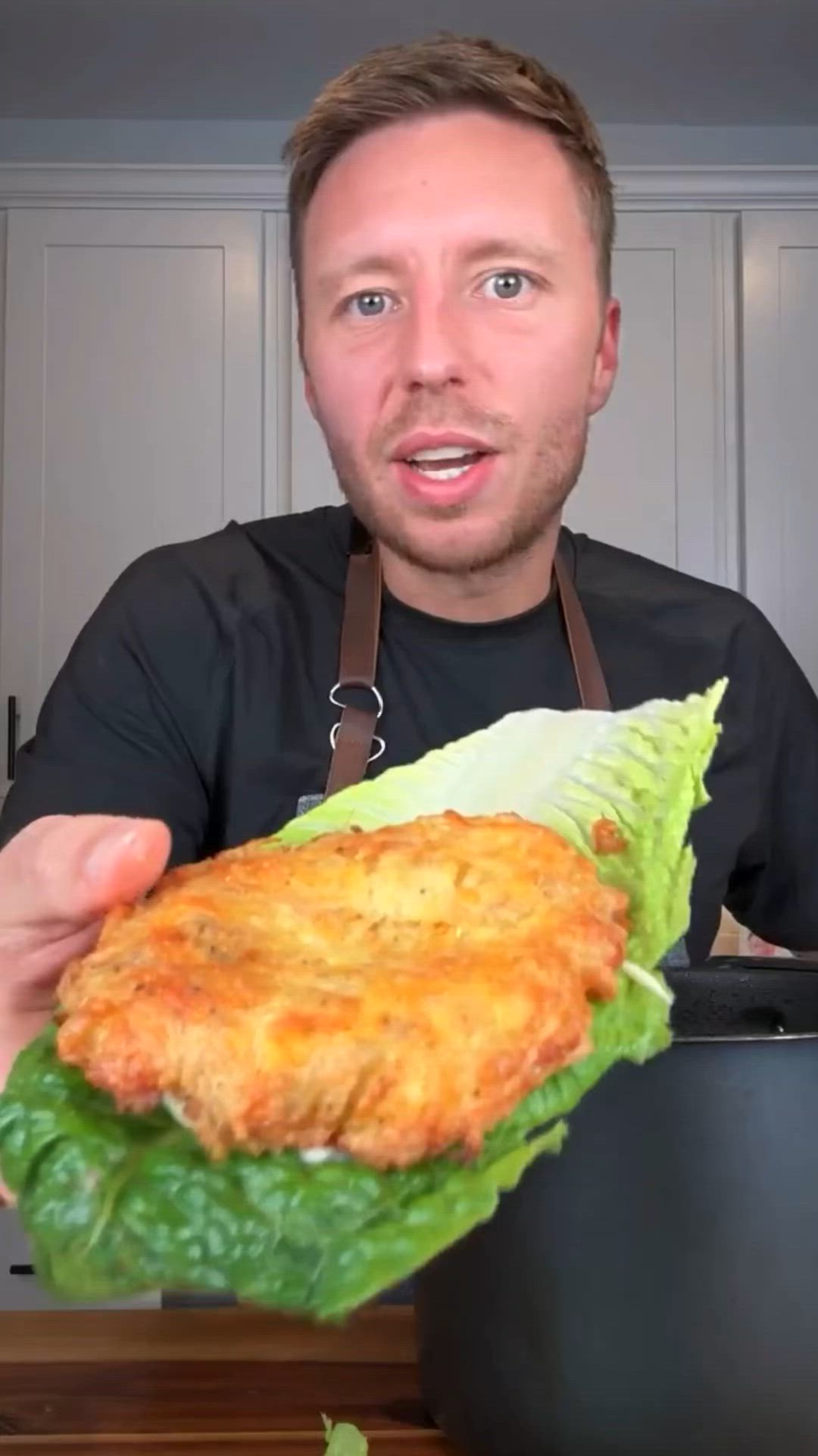 This may contain: a man in an apron is holding up a large sandwich with lettuce and cheese