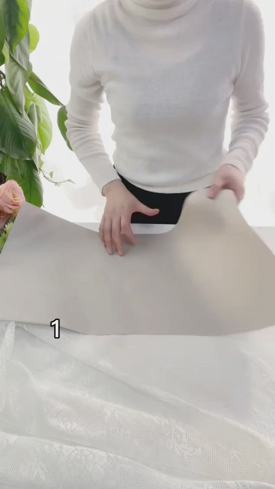 This may contain: a woman is cutting paper on a table with flowers and greenery in the background