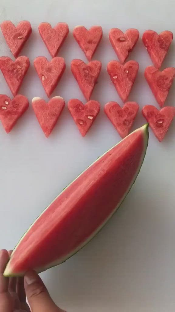 This may contain: someone is holding a slice of watermelon with hearts cut out of it to make them look like they are in love