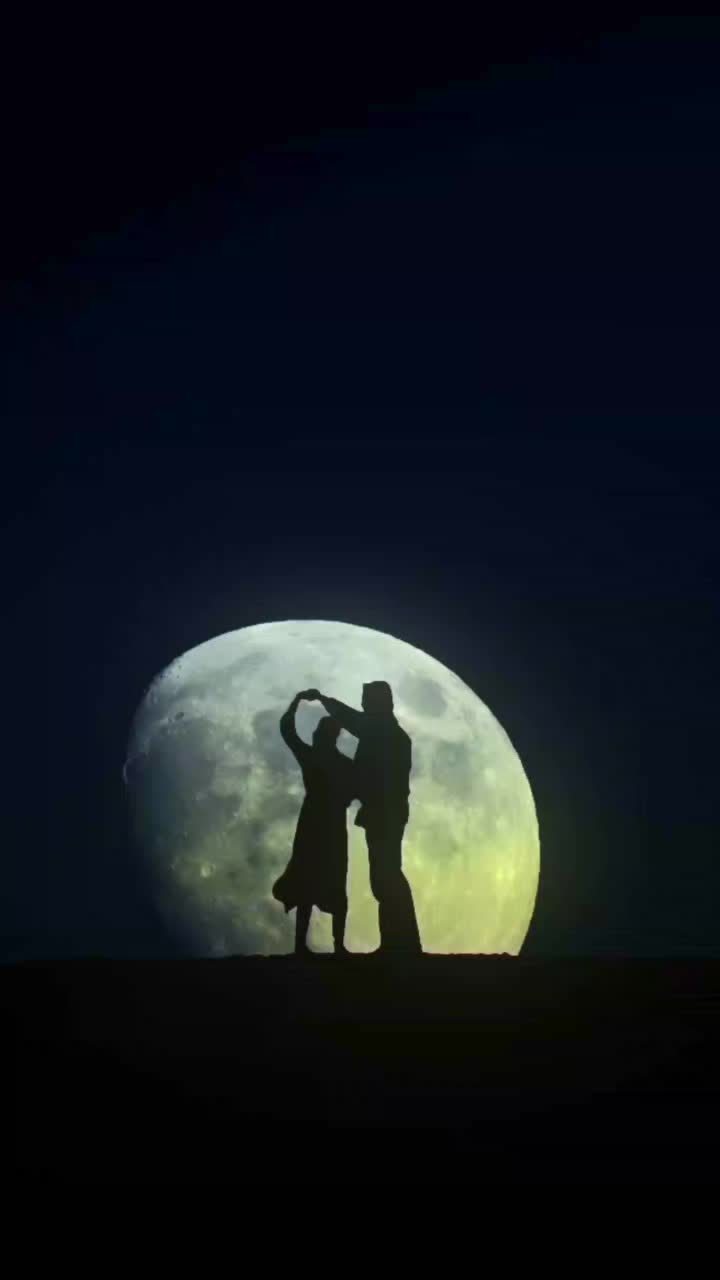 This may contain: two people are standing in front of the moon with their arms around each other's shoulders