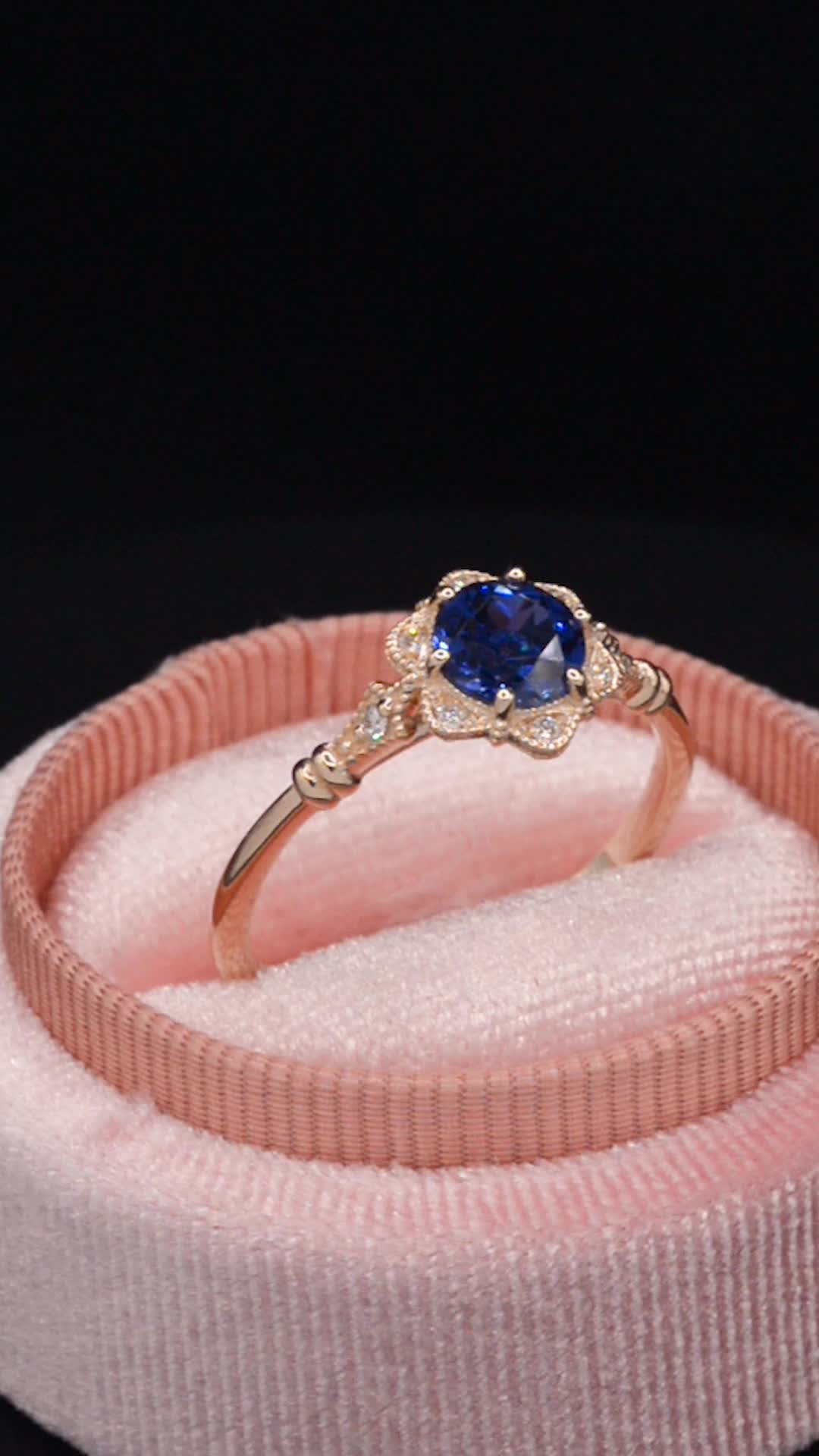 This may contain: a ring with a blue stone in it on top of a pink velvet band,