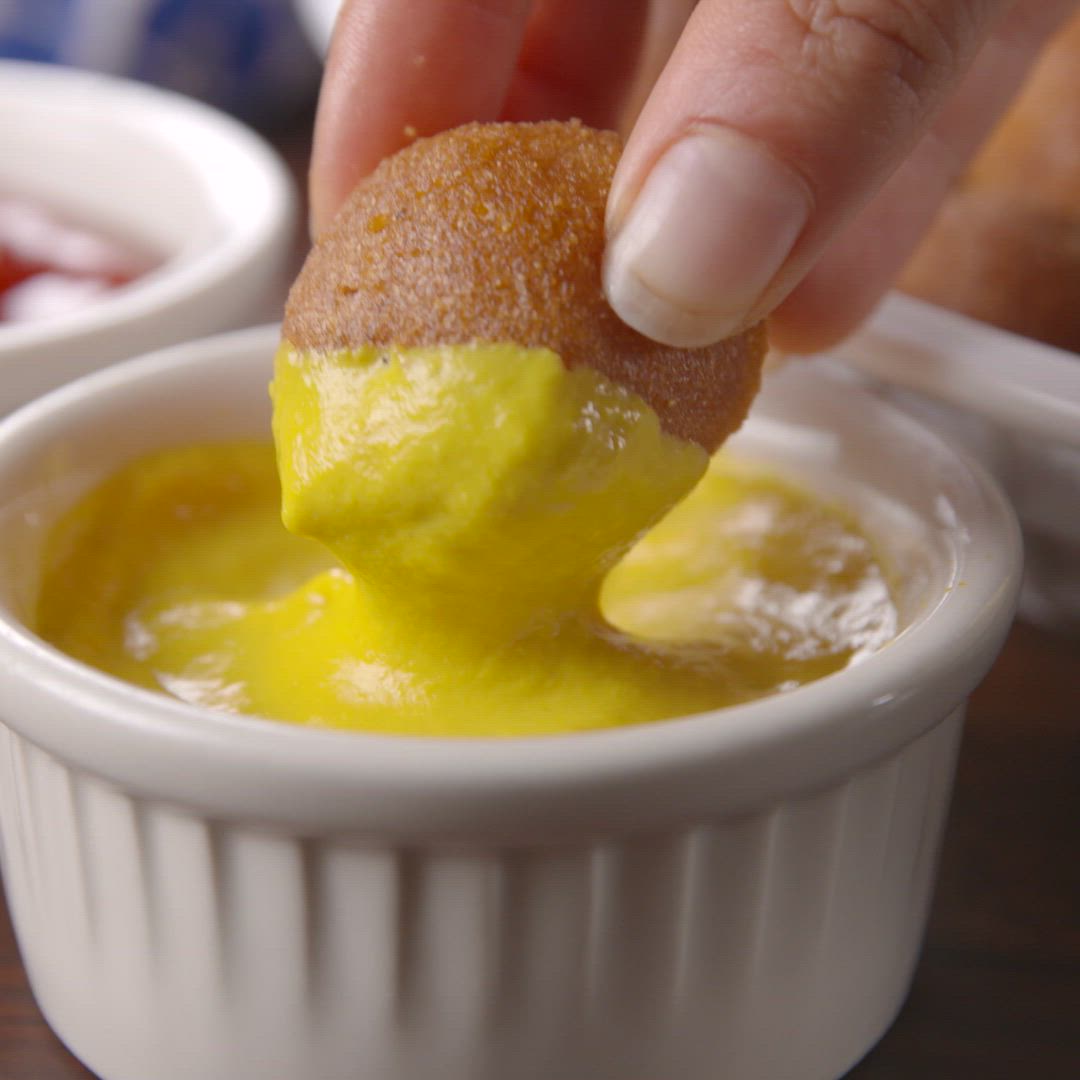 This may contain: a person dipping something into a small white bowl with yellow sauce in the middle,