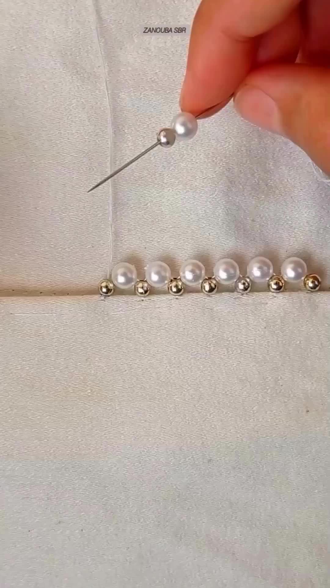 This may contain: the needle is being used to sew pearls on a white piece of cloth,