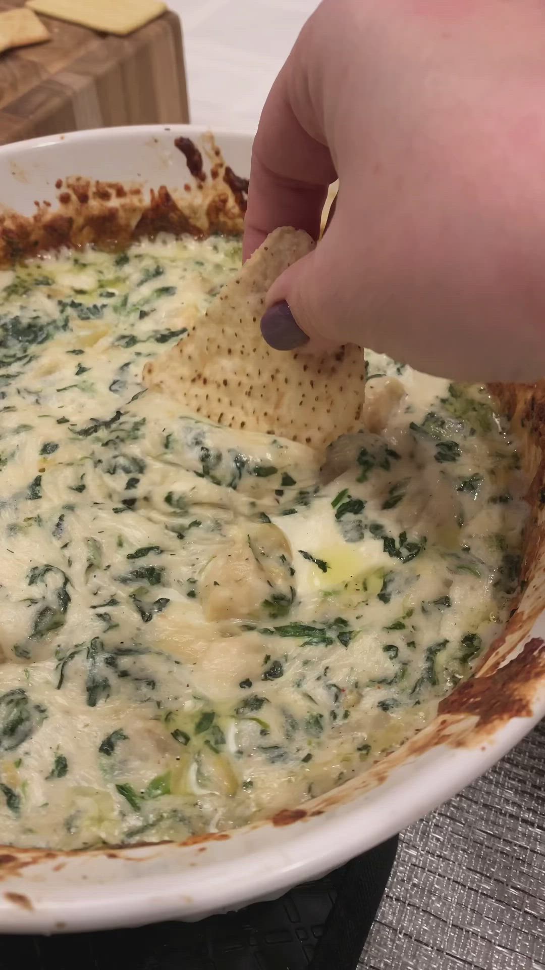 This may contain: a person dipping a tortilla chip into a bowl of spinach and cheese dip