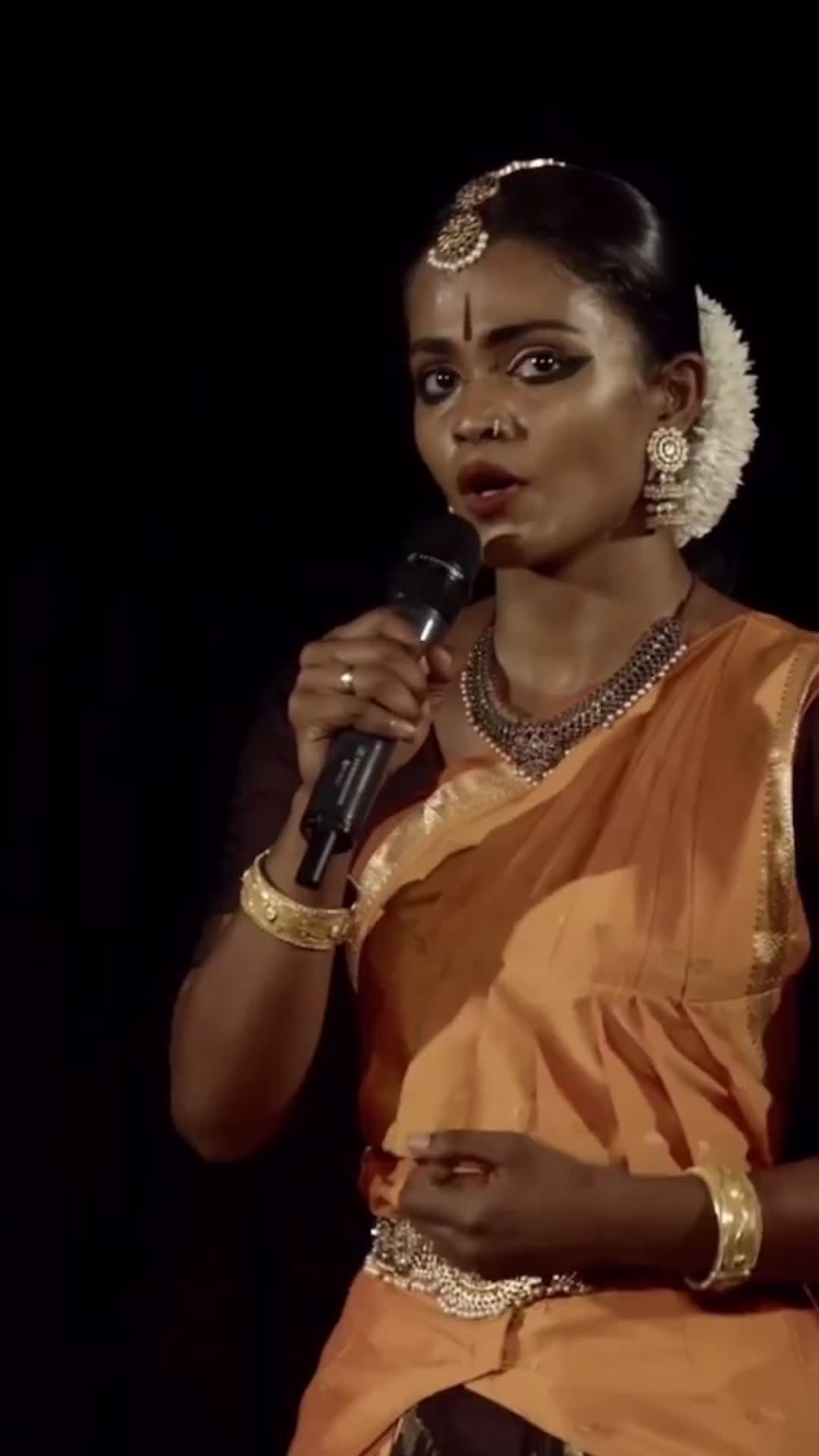 This may contain: a woman in an orange and gold sari with her hand on her hip, looking at the camera