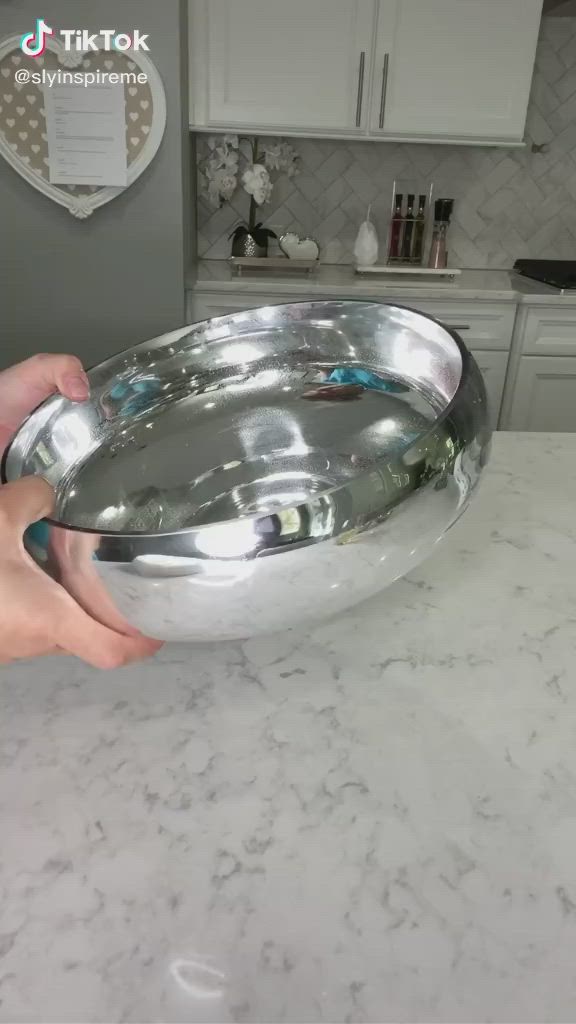 This may contain: a person holding a metal bowl on top of a marble countertop in a kitchen