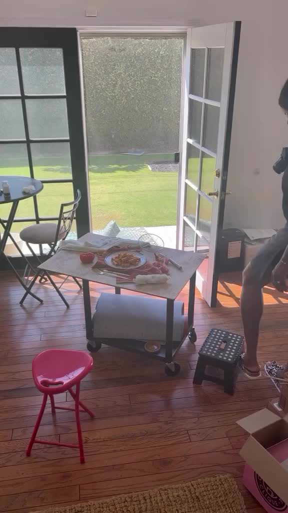 This may contain: a woman sitting on top of a pizza box in front of a sliding glass door