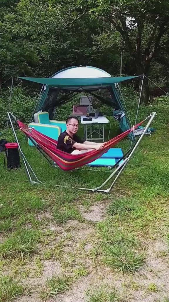 This may contain: a man laying in a hammock on top of a grass covered field next to trees