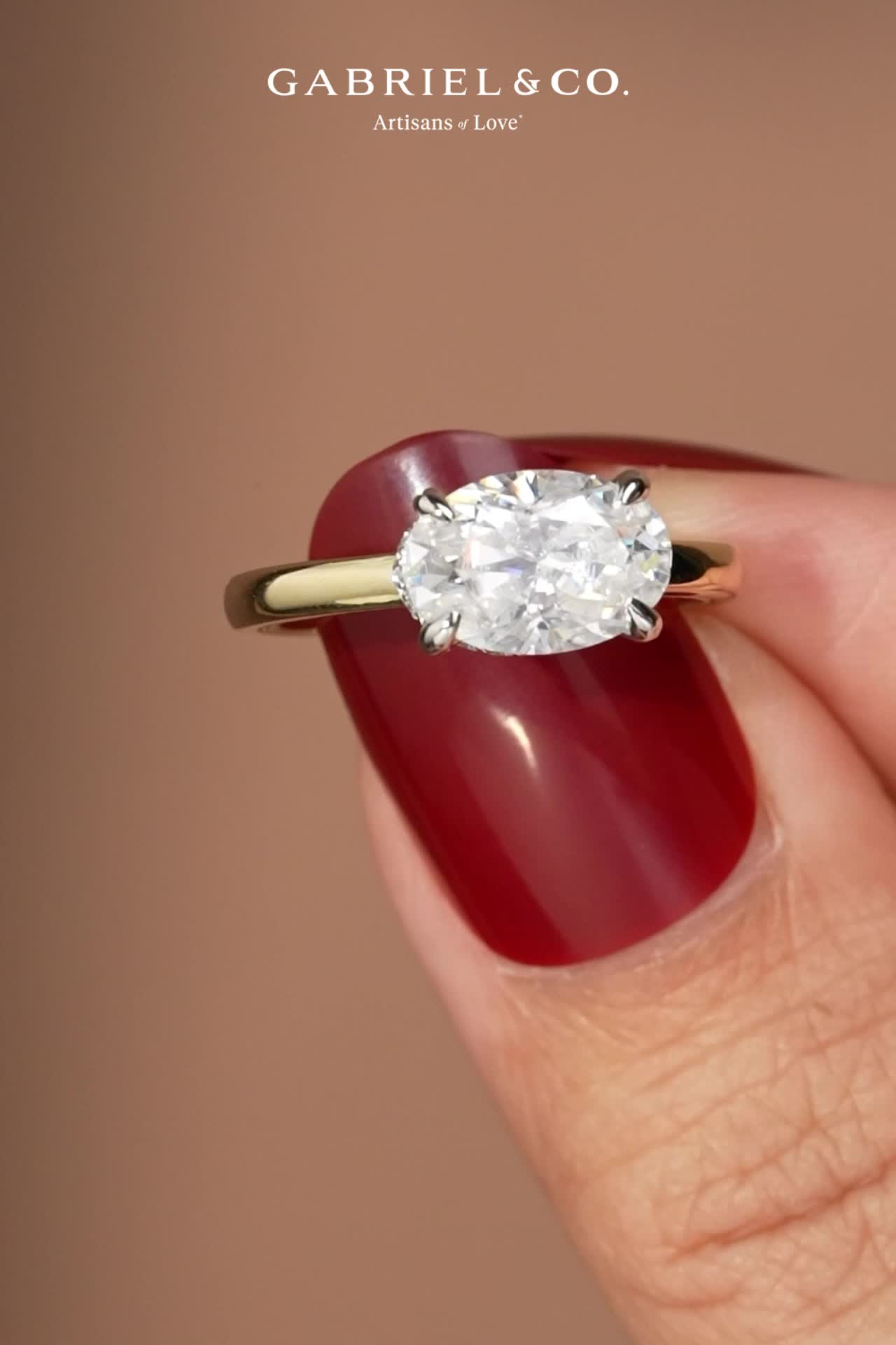 This may contain: a woman's hand holding a ring with an oval diamond on the middle finger