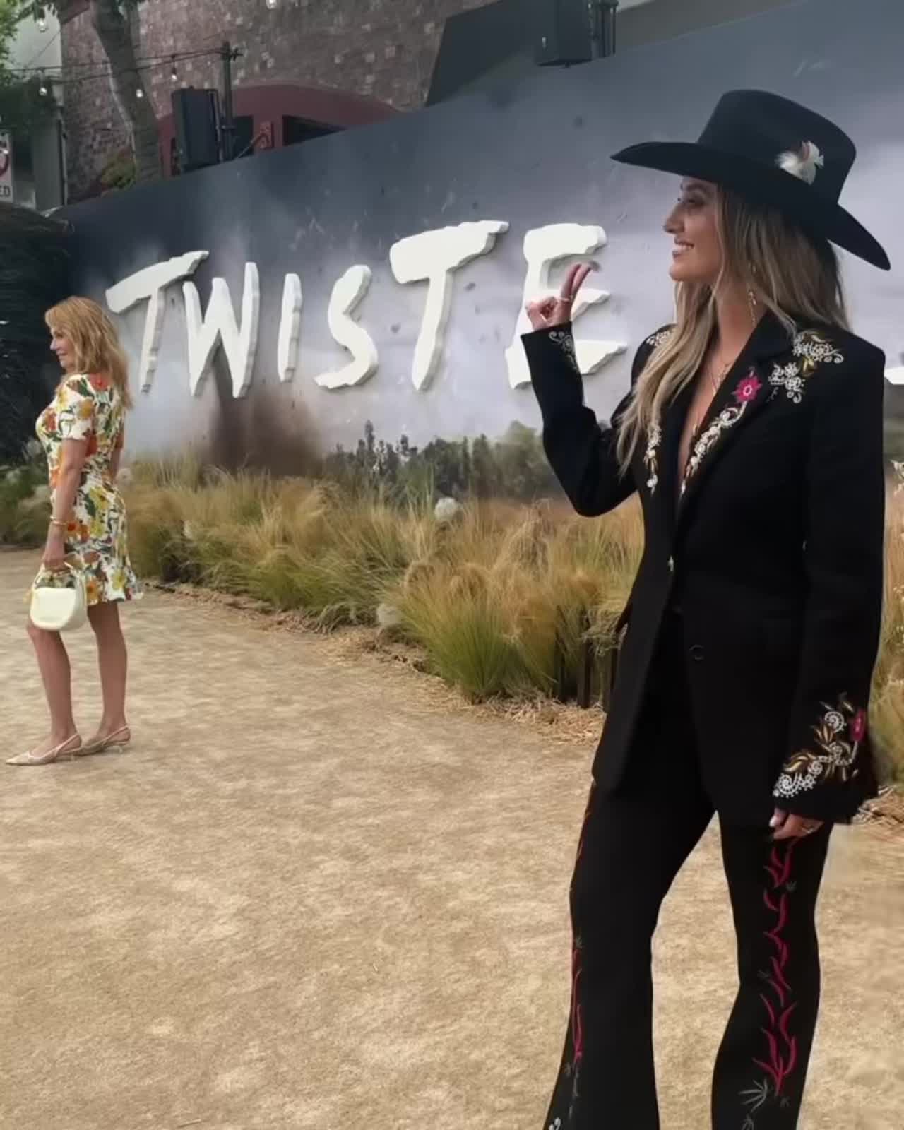 This may contain: two women standing in front of a sign with the word twiste on it and one woman wearing a black cowboy hat