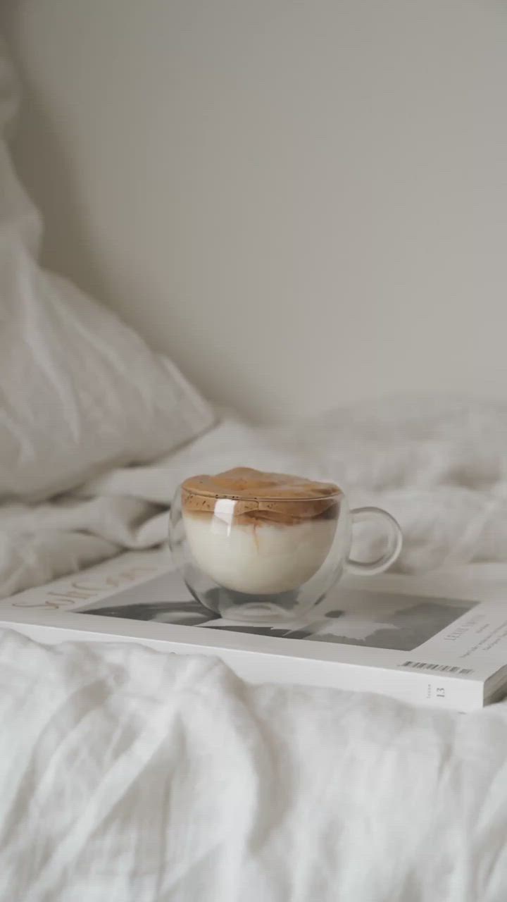 This may contain: a coffee cup sitting on top of a book in the middle of a bed with white sheets