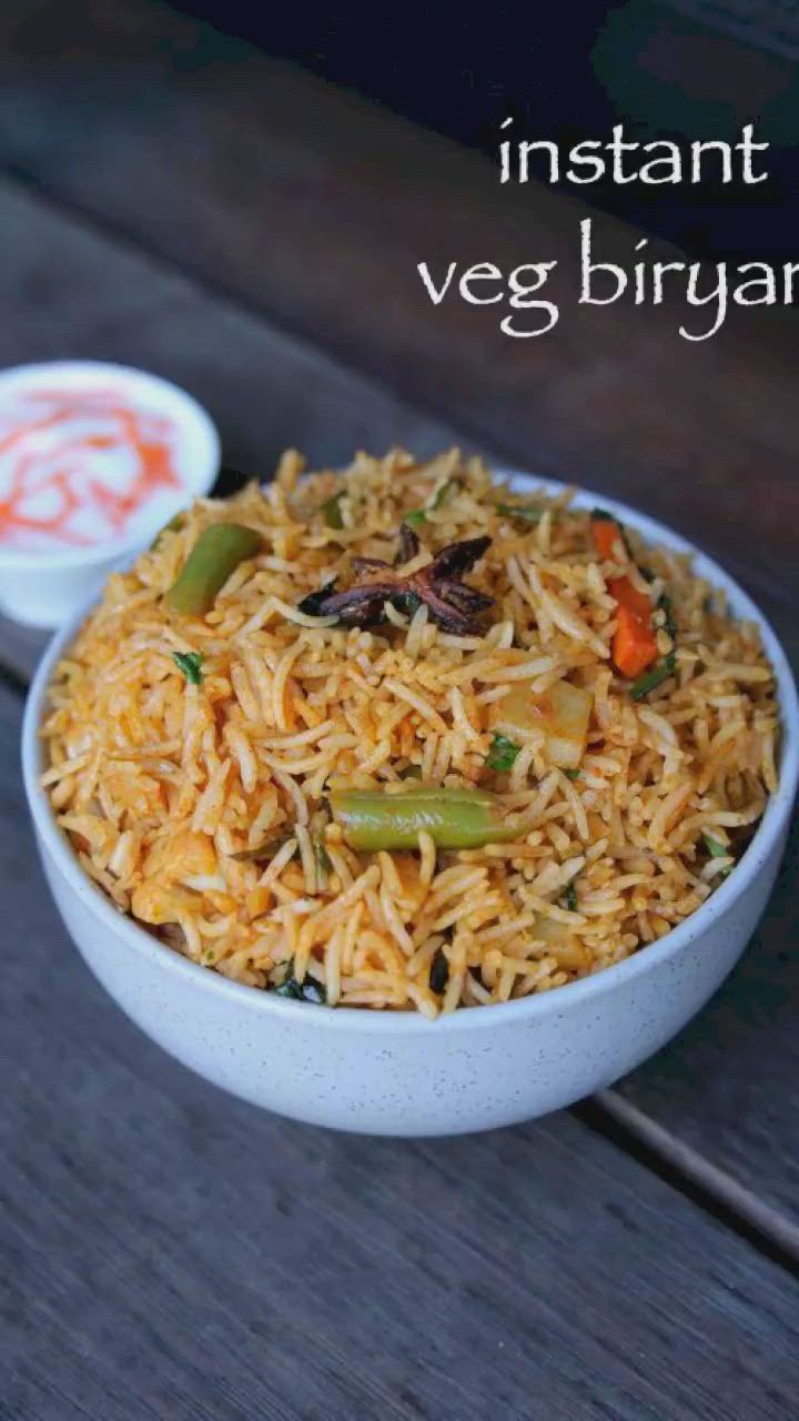 This may contain: a white bowl filled with rice and vegetables next to a container of seasoning on a wooden table