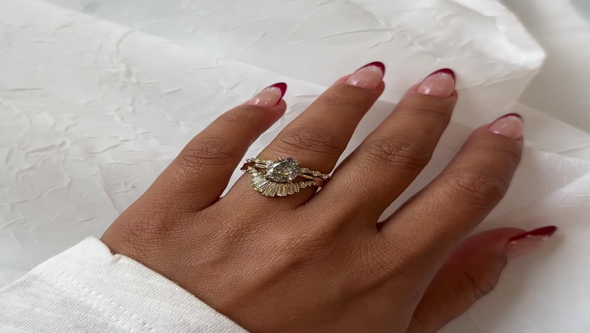 This may contain: a woman's hand wearing a gold ring with an oval diamond on top and leaves around the band