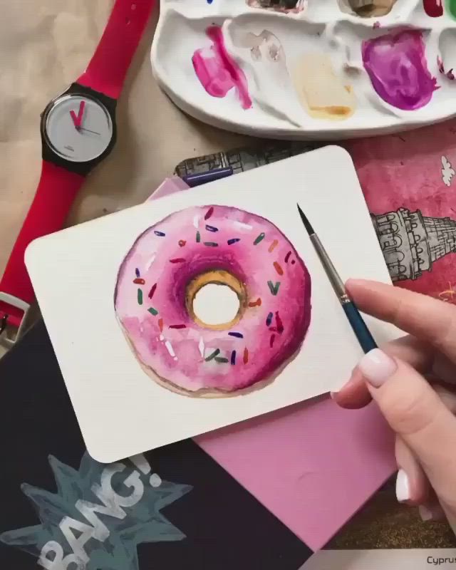 This may contain: a person is painting a donut with pink icing and sprinkles