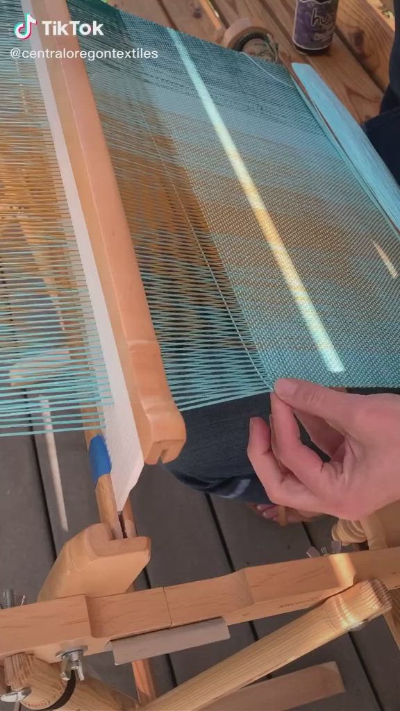 This may contain: someone is working on a weaving machine with blue yarn and wooden poles in the background