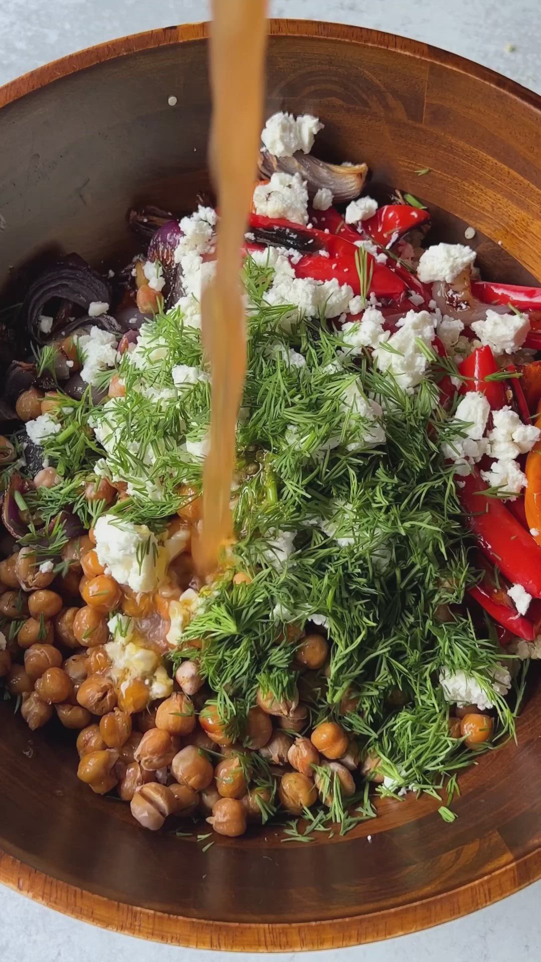 This may contain: a wooden bowl filled with vegetables and feta cheese being poured on top of it