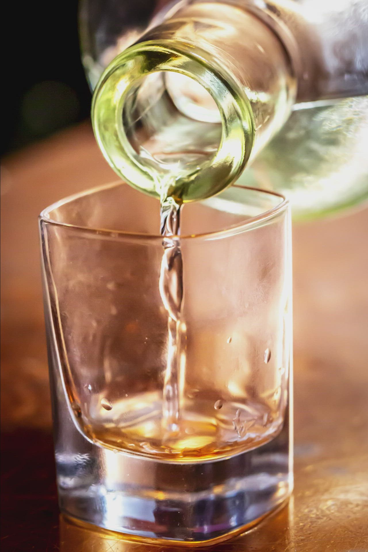 This may contain: a person pouring water into a glass on top of a wooden table next to a bottle