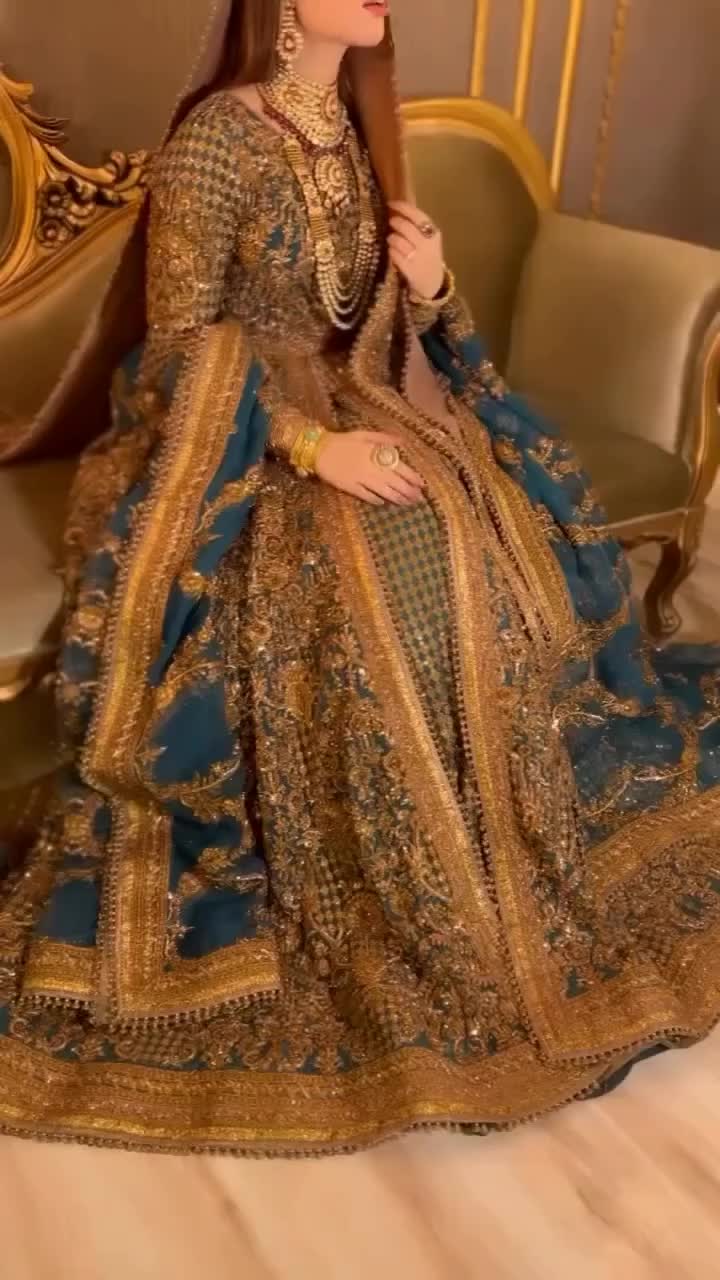 This may contain: a woman in a blue and gold wedding dress sitting on a couch with her hand under her chin