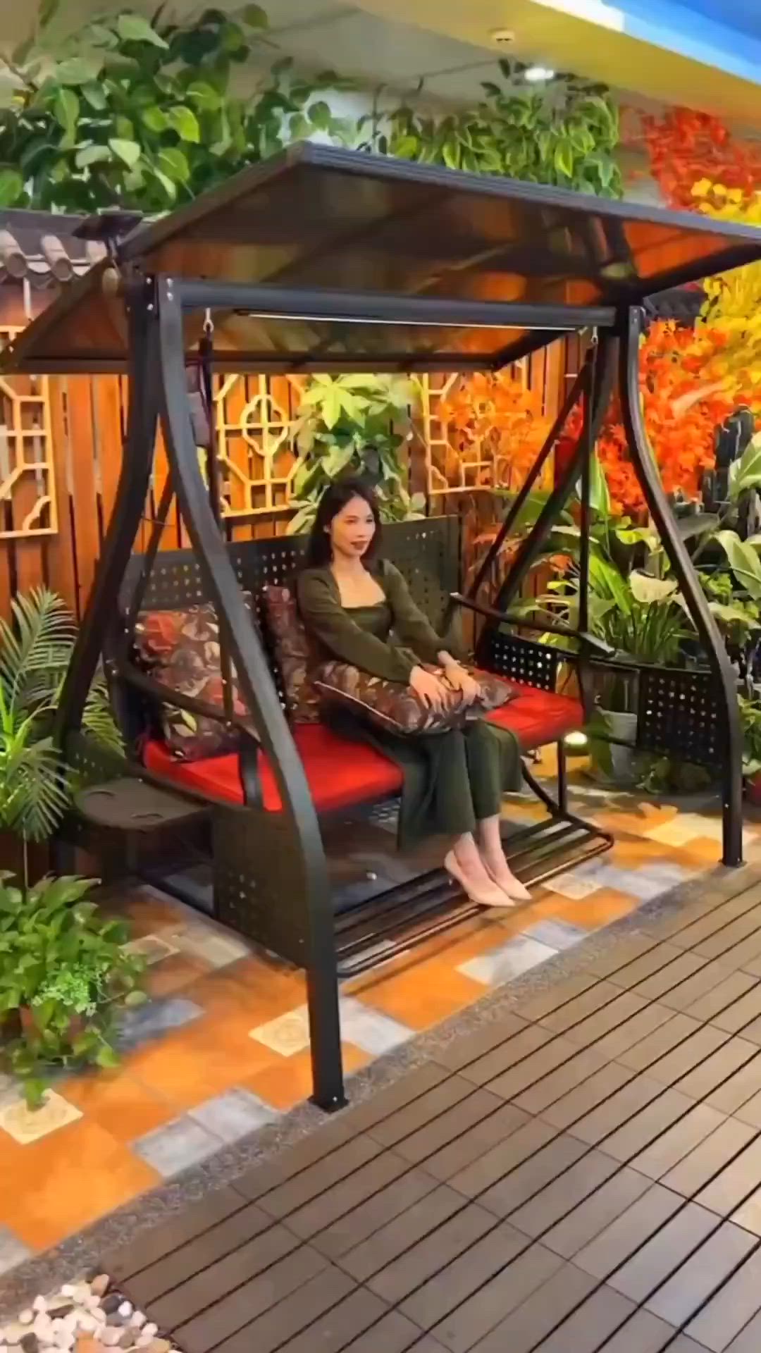 This may contain: a woman sitting on top of a swing chair in front of a tree and plants